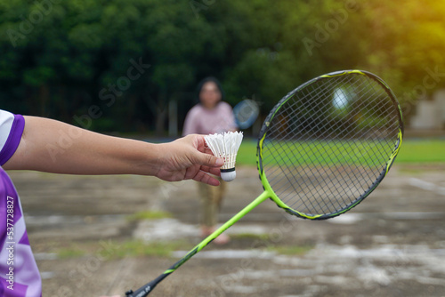 Asian woman and her friend badminton players play badminton together after work on courtyard at work. Concept, a leisure activity to do every day after work, soft and selective focus.