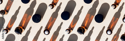 Banner made with brown glass bottle of cosmetic products and strong shadow on beige background, as a backdrop or texture. Creative layout for your design