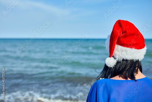 Woman in christmas Santa hat standing at the beach