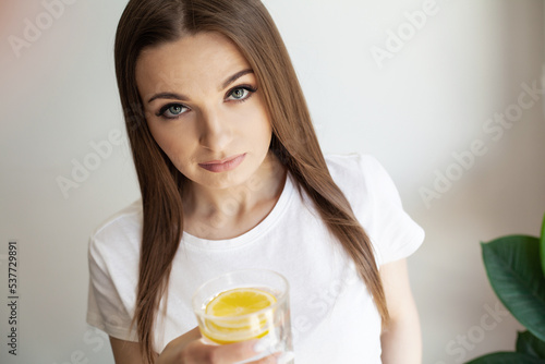 Beautiful young woman drinking fresh water with lemon at home