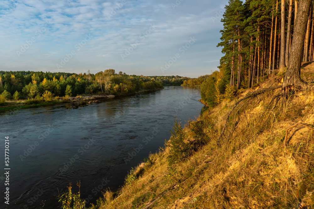 Autumn forest along the river and lake. The setting sun illuminates the treetops. Steep steep sandy bank above a wide river. Autumn walks in ecologically clean places. Autumn forest along the river and lake. The setting sun illuminates the treetops. Steep steep sandy bank above a wide river. Autumn walks in ecologically clean places.