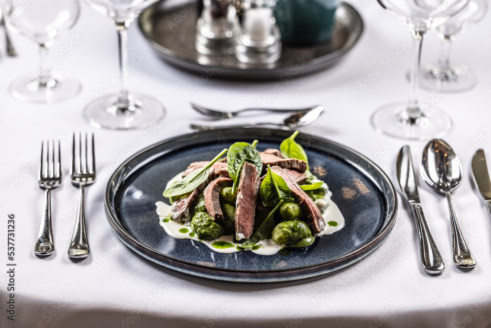 Creatively cooked beef flank steak with spinach gnocchi served on a ceremonially prepared table in the hotel restaurant Creatively cooked beef flank steak with spinach gnocchi served on a ceremonially prepared table in the hotel restaurant