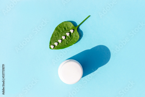 White pills on green plantain leaf and of bottle on blue background. Homeopathy, naturopathy, nutraceuticals and healthcare concept. Top view Flat lay photo
