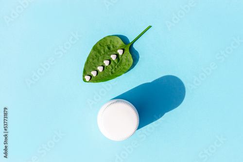 White pills on green plantain leaf and of bottle on blue background. Homeopathy, naturopathy, nutraceuticals and healthcare concept. Top view Flat lay
