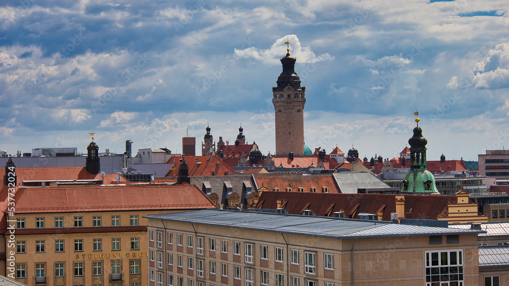 Obraz premium Blick über die Dächer der Innenstadt mit dem markanten Turm des Neuen Rathauses unter dramatischem Wolkenhimmel, Leipzig, Sachsen, Deutschland