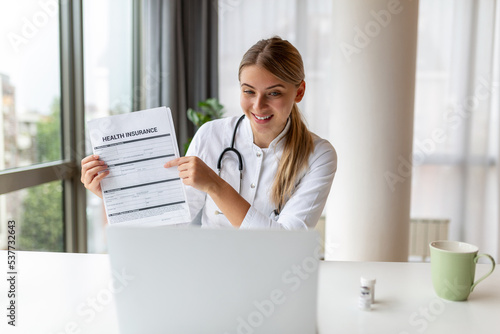 Attractive female doctor talking while explaining health insurance to patient through a video call with laptop in the consultation.