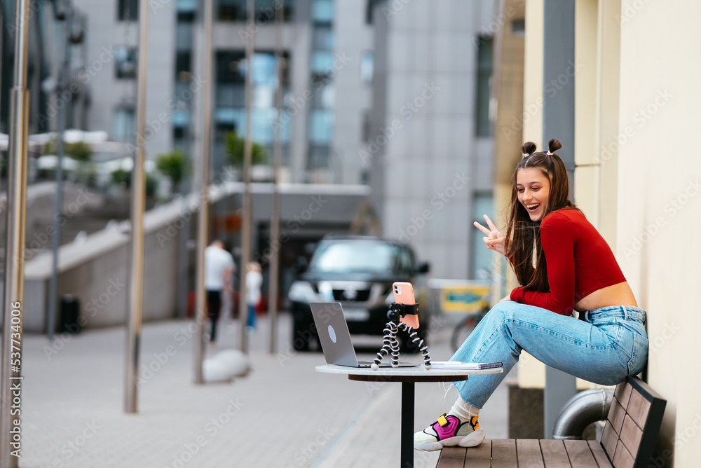 Fototapeta premium Woman blogger in a summer cafe streaming on the street.