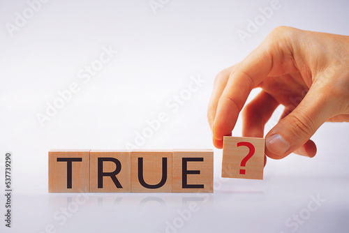 Wooden cubes with the word TRUE, the hand puts a cube with an exclamation mark. The concept of the question, the task, knowledge, lies.
