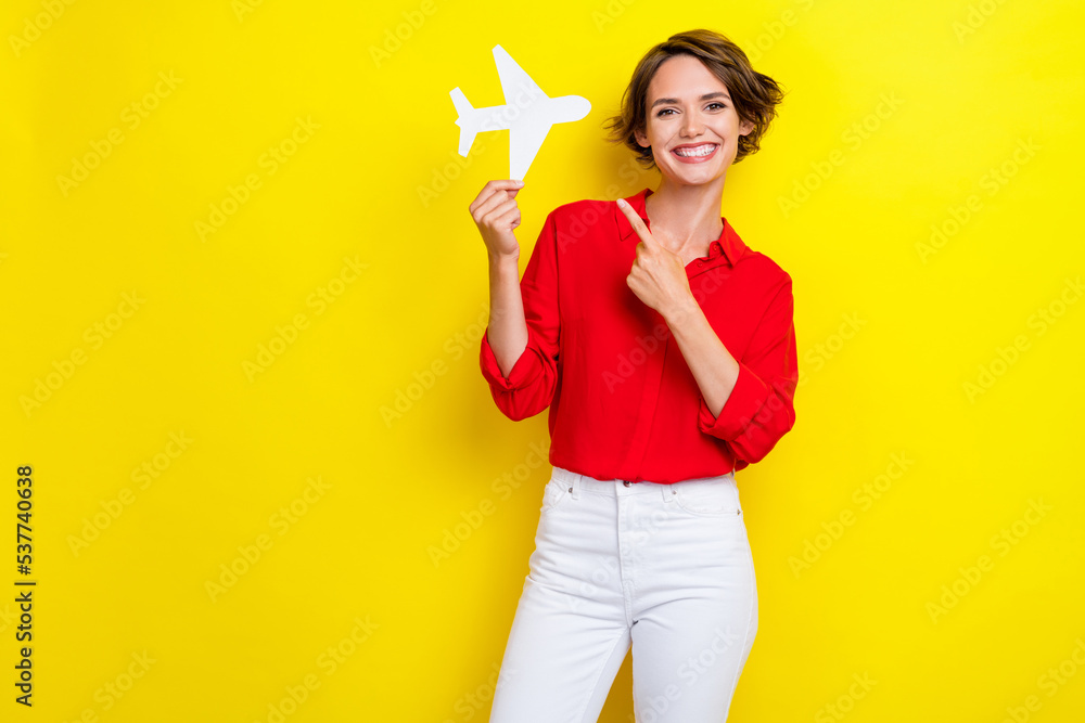 Photo of cheerful pretty lady indicate finger hand hold paper plane isolated on yellow color background Photo of cheerful pretty lady indicate finger hand hold paper plane isolated on yellow color background