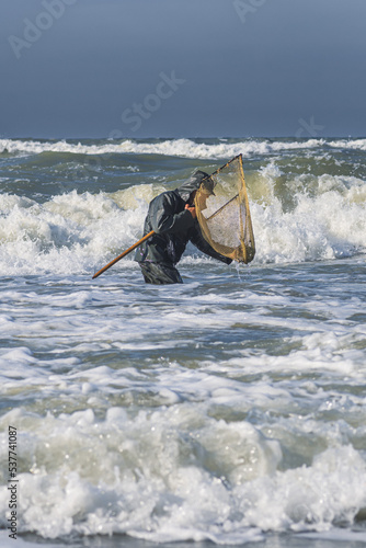 Amber catching in the Baltic Sea. Amber catcher or fisherman with fisherman's coat and boots into the sea among big waves using a scooping or fishing net, vertical photo