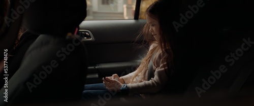 Fotografia, Obraz Portrait of cute little girl using her phone on the back seat while taking a ride to school