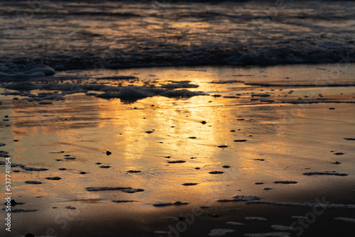 Beautiful sunset reflected on the sandy beach on the Baltic Sea with waves and reflections on the water