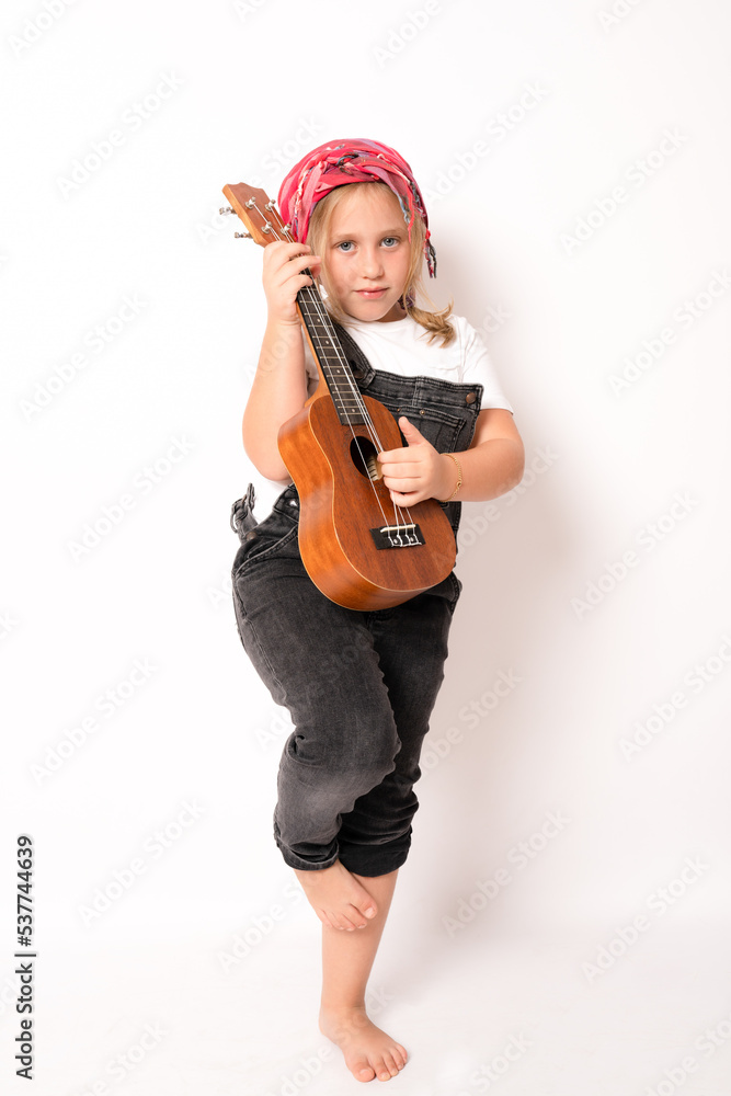 little girl in denim clothing playing the ukulele against white studio background little girl in denim clothing playing the ukulele against white studio background