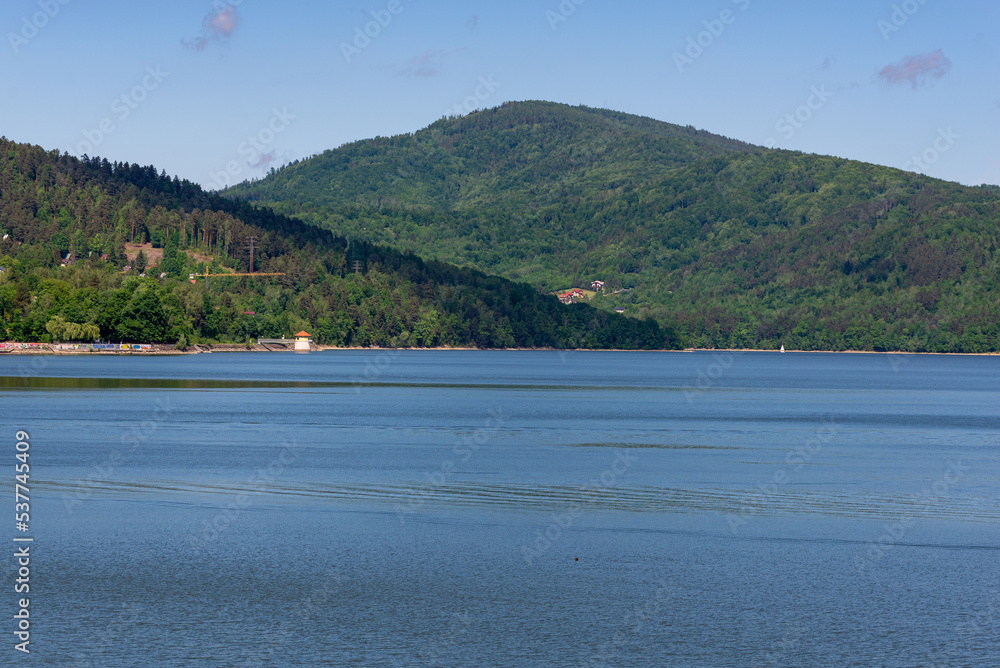 Zarzecze, śląskie, Polska, 05.28.2022. Jezioro Żywieckie. Chmury i góry w promieniach słońca, spokojna woda (). Zarzecze, śląskie, Polska, 05.28.2022. Jezioro Żywieckie. Chmury i góry w promieniach słońca, spokojna woda ().