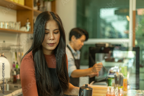 Female business owner works with her partner to prepare coffee or drink for customer in a coffee shop. A couple of LGBT startup help each other at a coffee counter for their business.