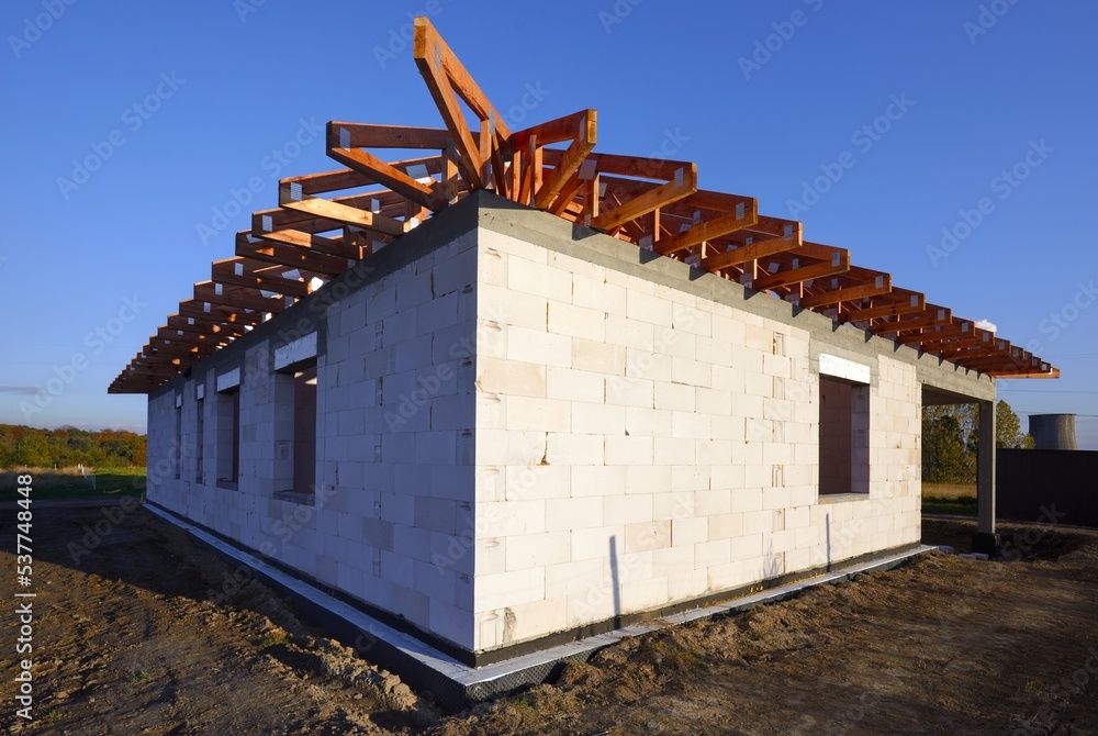 Dom jednorodzinny w budowie w stanie surowym z widoczną drewnianą kontrukcją dachu - obrazy, fototapety, plakaty 