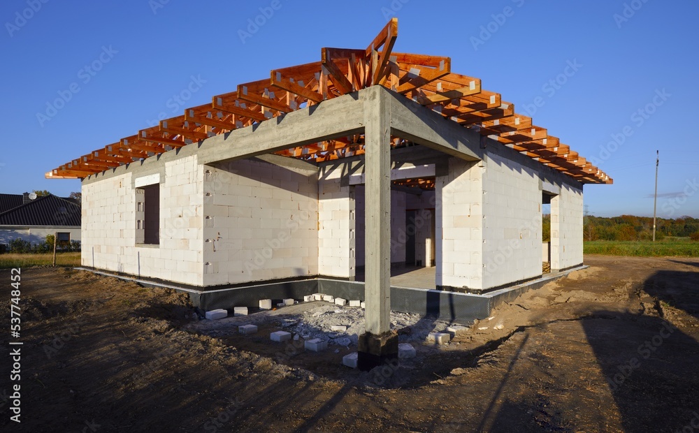 Dom jednorodzinny w budowie w stanie surowym z widoczną drewnianą kontrukcją dachu - obrazy, fototapety, plakaty 