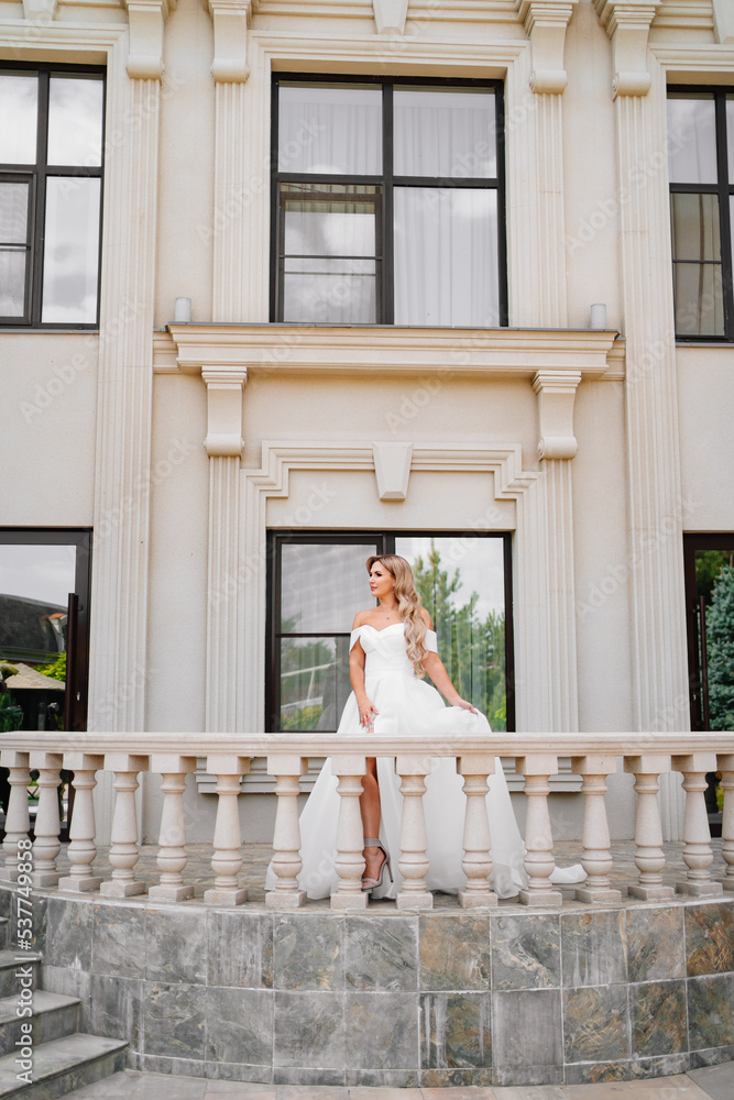 beautiful bride blonde in a white dress at the railing of the classical building