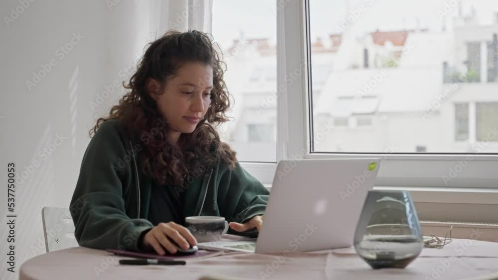 Working from home woman looks outside the window and then to her computer. Relaxed at home with casual clothes young female is sitting by table enjoying working from her apartment. Remote or digital Working from home woman looks outside the window and then to her computer. Relaxed at home with casual clothes young female is sitting by table enjoying working from her apartment. Remote or digital