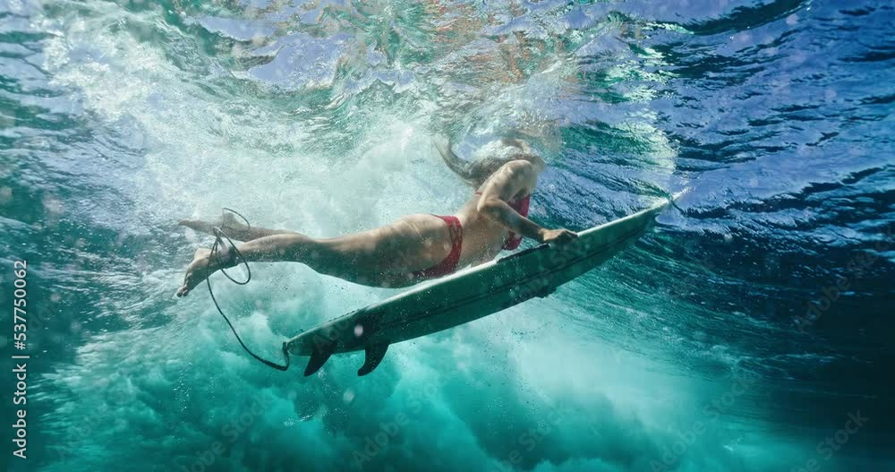 Surfer girl dives under large ocean wave on surfboard, underwater view of woman duck diving Surfer girl dives under large ocean wave on surfboard, underwater view of woman duck diving