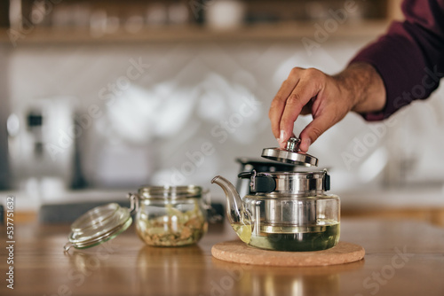 Male person holding a teapot, ready to drink tea, at home.