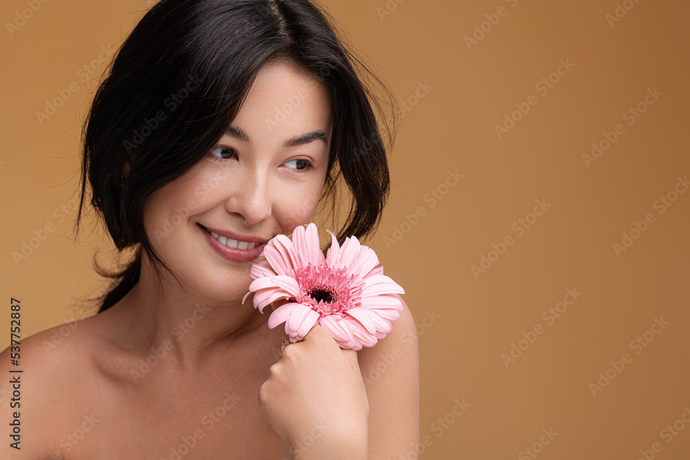 Content young Asian lady with fresh flower in hand smiling in studio Content young Asian lady with fresh flower in hand smiling in studio