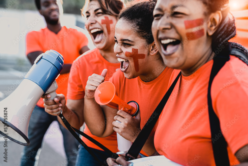 Obraz premium Females football fans exulting while watching soccer game at stadium - Women with painted face and megaphone encouraging their team - Sport entertainment concept