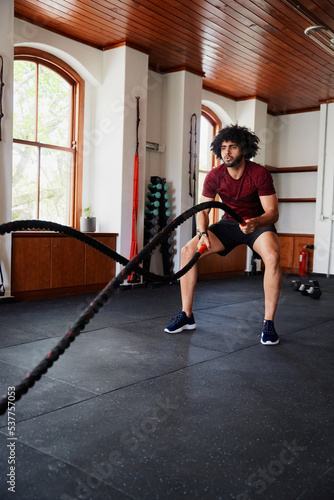 Focused young middle eastern man doing battle ropes exercises at the gym