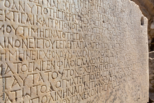 Fragment of ancient greek inscription, carved on marble block at the archaeological site of Ephesus. Selcuk, Turkey (Turkiye). Selected focus. Ancient art and history concept. Retro background © Elena