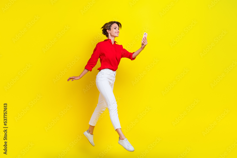 Full length photo of crazy carefree person jumping hold use telephone isolated on yellow color background
