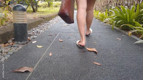 An asian young woman wear red dress carrying beach tote bag walking on pathwat to the beach paradise in summer vacation in slowmotion photo