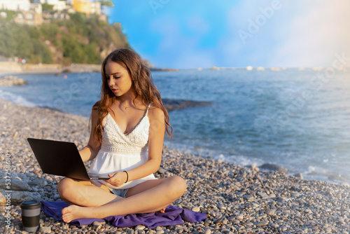Teenage girl works on computer and talks on phone on the beach. concept of work and vacation together, digital nomads around the world © Natalia