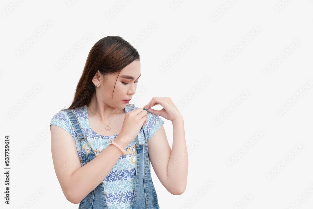 A Southeast Asian lady adjusts the straps of her lightwashed denim jumper. Isolated white background studio shot. A Southeast Asian lady adjusts the straps of her lightwashed denim jumper. Isolated white background studio shot.
