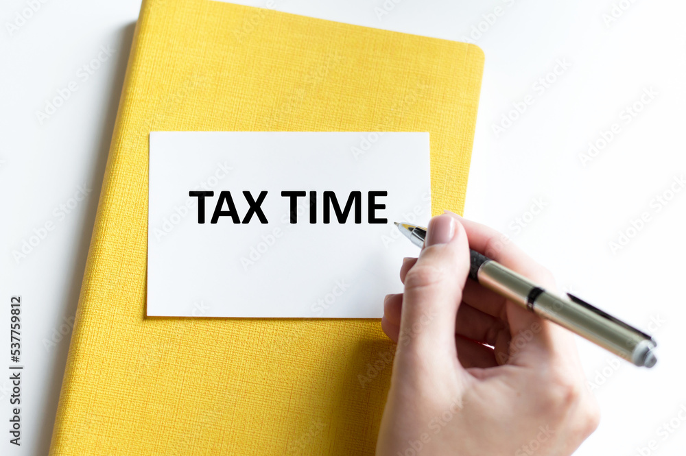 Tax time text on a card on a yellow notebook on a light background next to the hand of the businessman Tax time text on a card on a yellow notebook on a light background next to the hand of the businessman