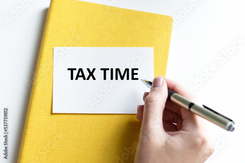 Tax time text on a card on a yellow notebook on a light background next to the hand of the businessman photo