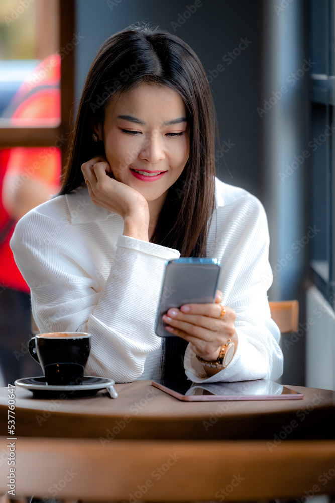 Young asian woman happy face smiling and using with mobile smartphone in cafe. Woman holding phone and looking at mobile smartphone and surfing the internet, chatting, blogging. Young asian woman happy face smiling and using with mobile smartphone in cafe. Woman holding phone and looking at mobile smartphone and surfing the internet, chatting, blogging.