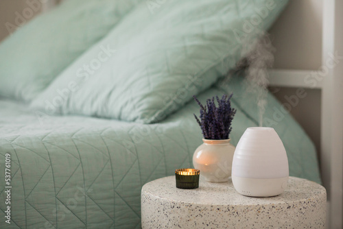 Modern aroma oil diffuser or humidifier on the table whith lavender flowers and a candle near the bed. Aromatherapy and relaxing. photo