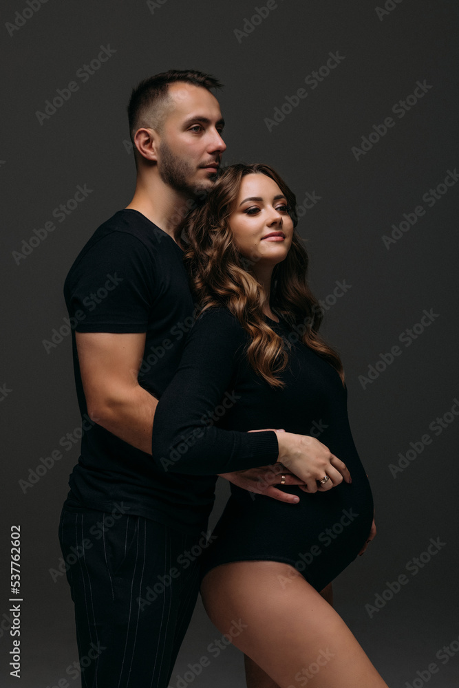 Handsome young pregnant couple posing on dark background. Handsome young pregnant couple posing on dark background.