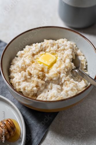 Unusual healthy delicious rice pudding made from brown rice and plant based milk served with butter and honey in grey bowl