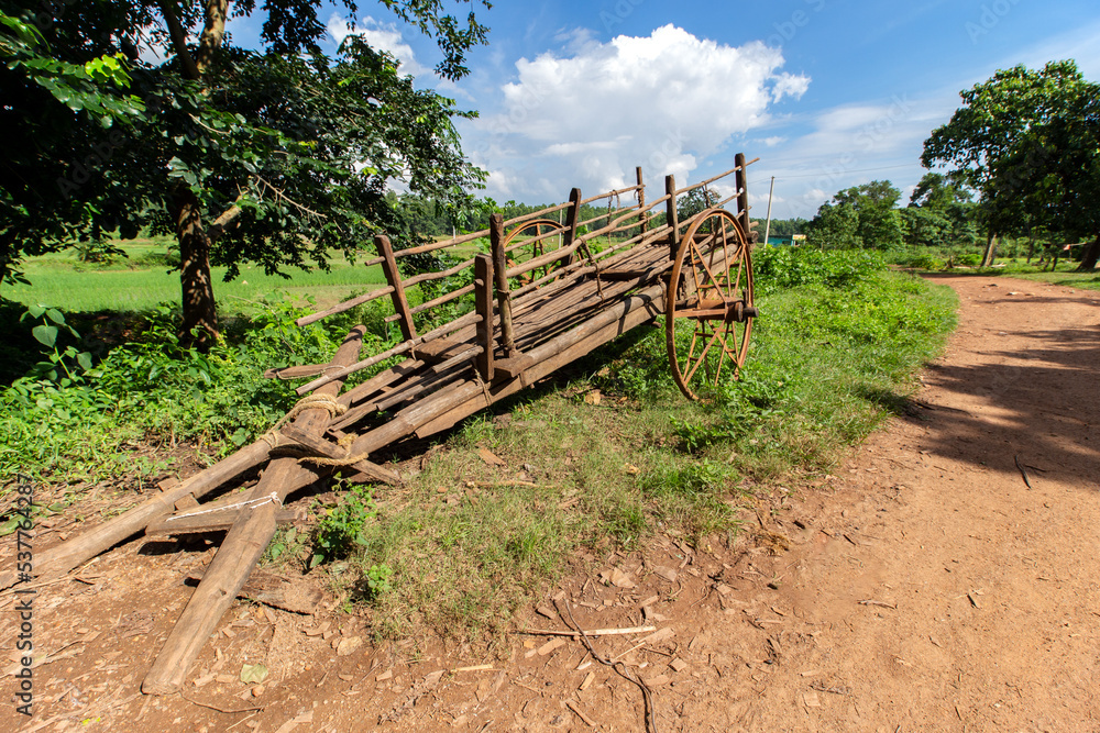 A traditional bullock cart on village road of Bengal. Paddy field on backside side of the road and small plateau hill in background. A traditional bullock cart on village road of Bengal. Paddy field on backside side of the road and small plateau hill in background.