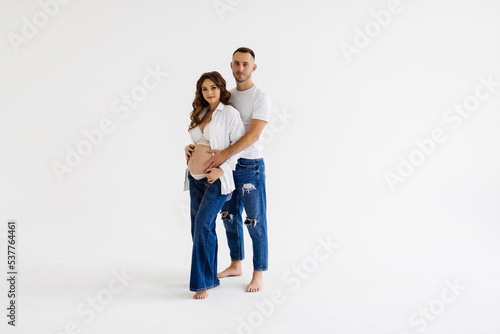 Cheerful young man standing with his pregnant woman isolated over white background wall. Looking aside.