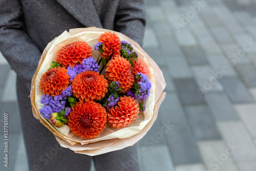 A person in grey coat holding beautiful bouquet of orange dahlia flowers. photo