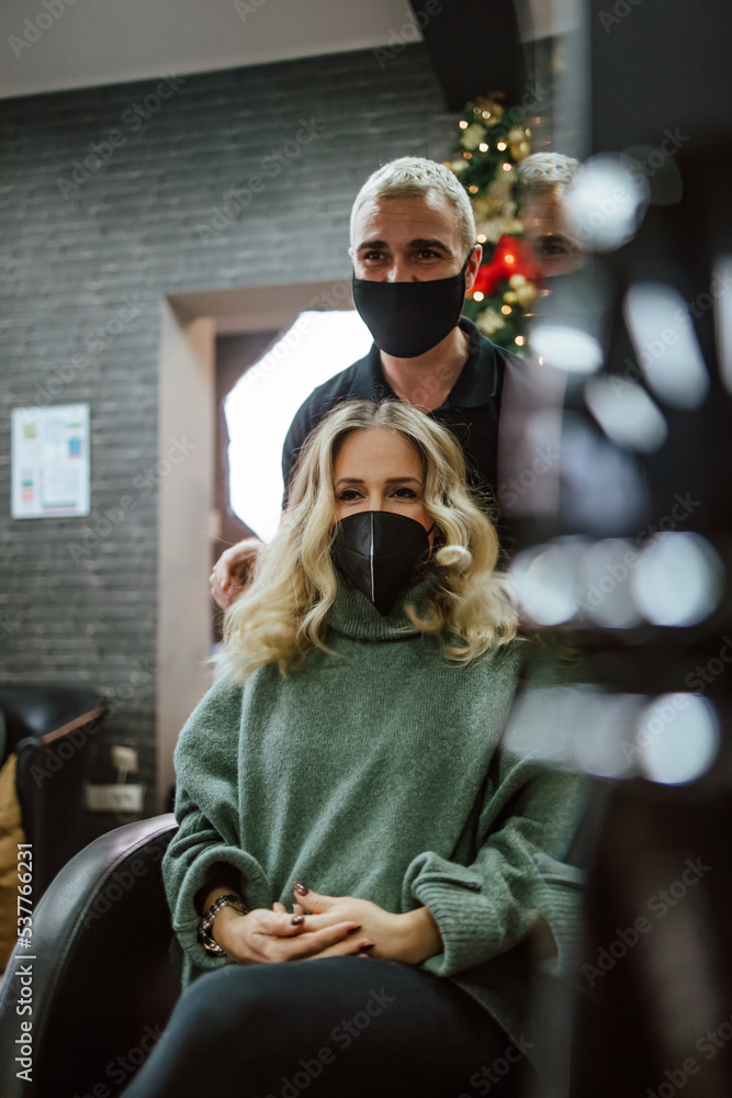 Fototapeta premium Beautiful hairstyle of woman after dyeing hair and making highlights in hair salon. She is wearing protective face mask as protection against virus pandemic.