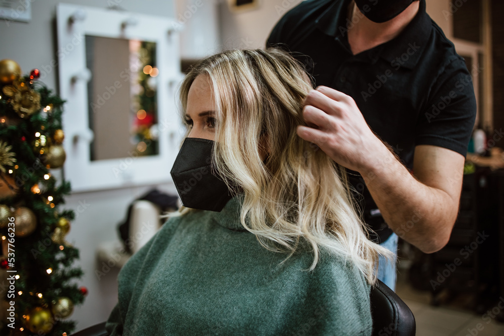 Fototapeta premium Beautiful hairstyle of woman after dyeing hair and making highlights in hair salon. She is wearing protective face mask as protection against virus pandemic.