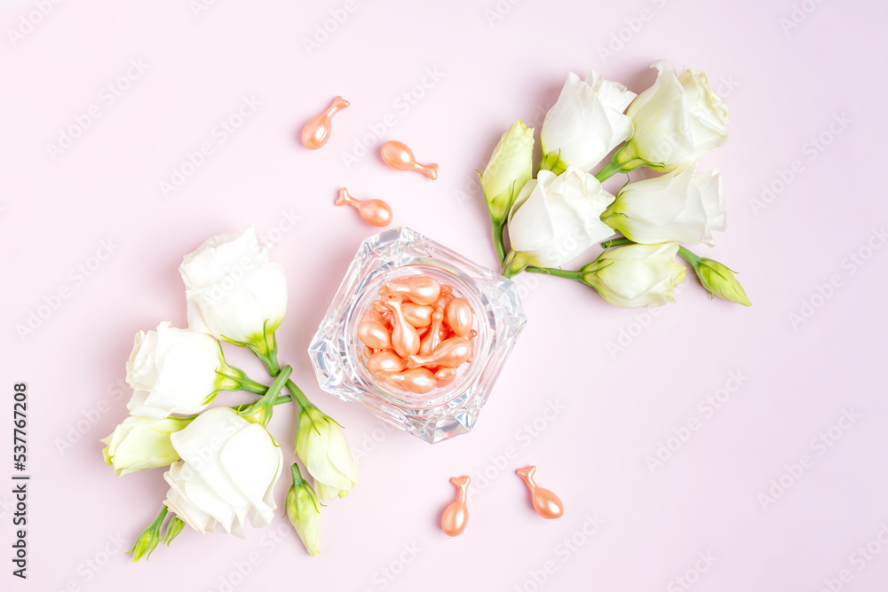 Rose Gold capsules with cosmetic oil for face in glass jar with eustoma flowers composition on pink background. Singl use packege. Travel cosmetics. Concept