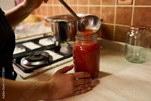Close-up. Chef using a ladle, pours boiling juice of organic juicy tomatoes into a sterilized canning can. Preparing tomato sauce or passata. Preserving homegrown vegetables for winter. Canned food