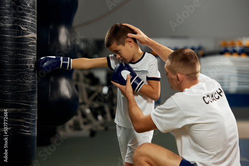 Training in boxing techniques. Junior male boxer practicing with personal coach at sports gym  indoors. Concept of studying  challenges  sport  hobbies  competition