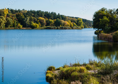 Beautiful autumn landscape. Pine and deciduous forest, clear lake and blue sky. Autumn in Chernigov, Ukraine © Julia