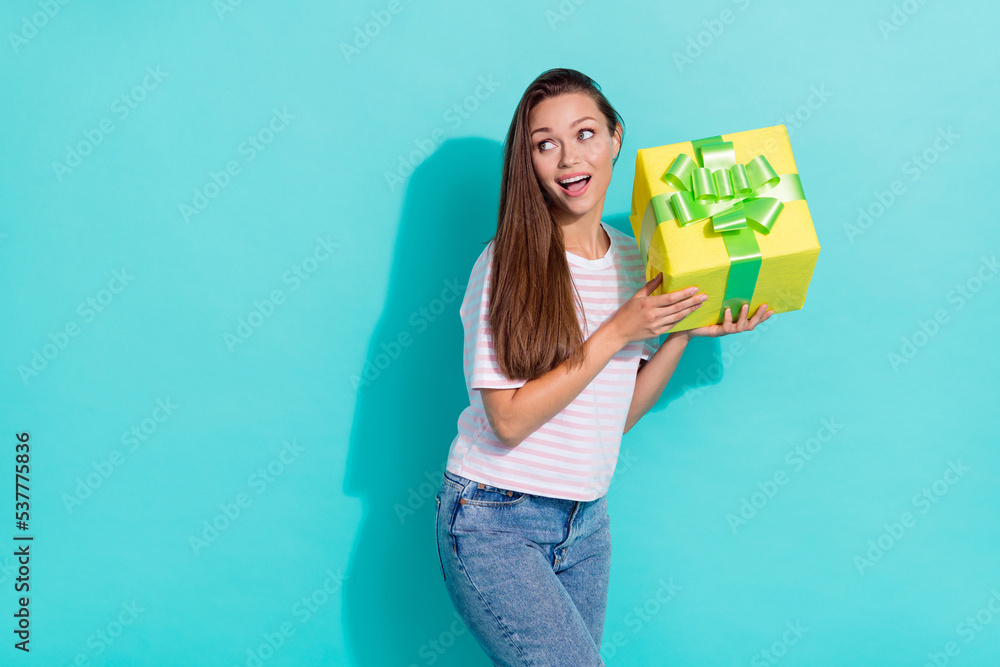 Photo of adorable lovely positive woman wear striped t-shirt hold yellow present look empty space isolated on teal color background Photo of adorable lovely positive woman wear striped t-shirt hold yellow present look empty space isolated on teal color background