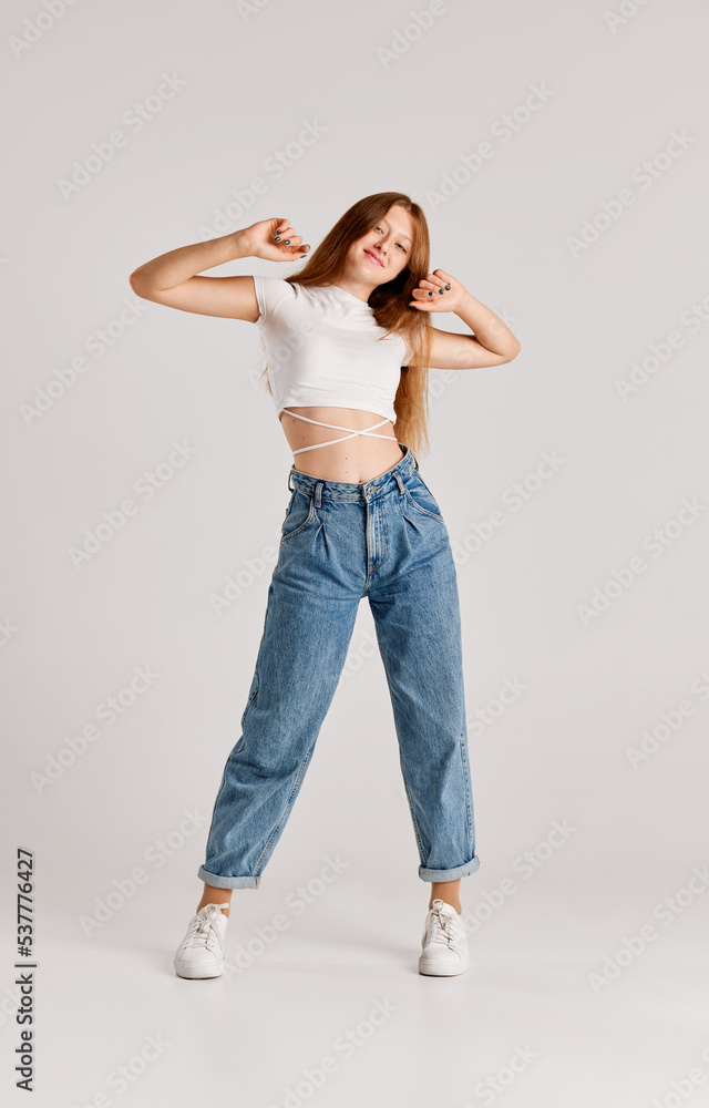 Full-length portrait of young beautiful redhead girl posing in casual clothes, jeans and white top over grey studio background Full-length portrait of young beautiful redhead girl posing in casual clothes, jeans and white top over grey studio background
